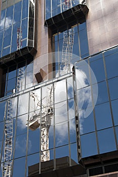 Reflection of crane from worksite in exterior of glass office building