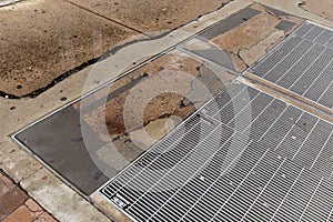 Urban sidewalk with heavy metal grates, cracked concrete with multiple patched areas