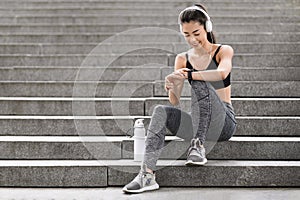 Urban Sport Concept. Smiling Asian Girl Checking Smartwatch Settings Before Jogging Outdoors