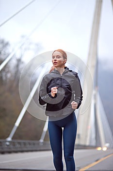 urban sports, confident young woman jogging in city at cold spring morning