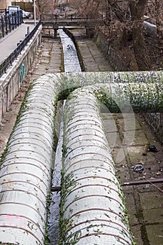 Urban stream. Industrial pipes. Concrete riverbed and river bank