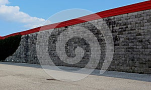 Urban street background. Asphalt road alongside a wall made of little concrete blocks with red edge on top