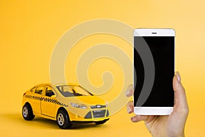 Urban taxi mobile online application concept. Toy yellow taxi car model. Hand holding smart phone with taxi service app