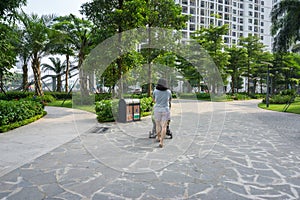 Urban walking road among green tree in modern apartment buildings in big city, with woman pushing baby stroller