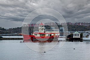 Urban winter scene with a red lighthouse light ship houseboat with dramatic clouds and buildings in the background.