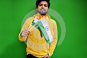 Urban young hipster indian man in a fashionable yellow sweatshirt hold flags of India in hands. Cool south asian guy wear hoodie