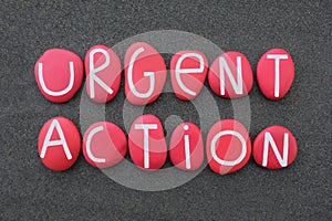 Urgent action text composed with red colored stone letters over black sand