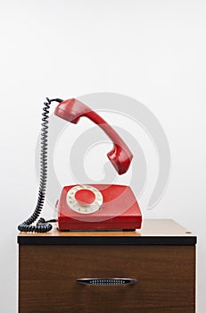 Red retro telephone on wooden nightstand