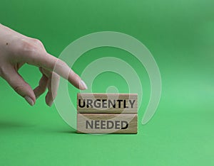 Urgently needed symbol. Concept word Urgently needed on wooden blocks. Beautiful green background. Businessman hand. Business and