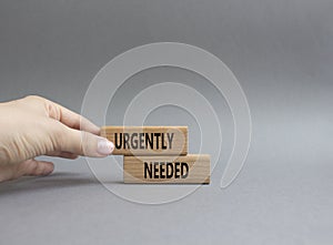 Urgently needed symbol. Concept word Urgently needed on wooden blocks. Beautiful grey background. Businessman hand. Business and