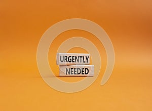 Urgently needed symbol. Concept word Urgently needed on wooden blocks. Beautiful orange background. Business and Urgently needed