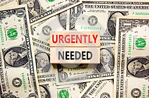 Urgently needed symbol. Concept words Urgently needed on wooden blocks on a beautiful background from dollar bills. Business and