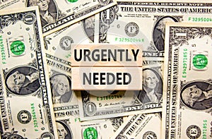 Urgently needed symbol. Concept words Urgently needed on wooden blocks on a beautiful background from dollar bills. Business and