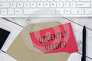 Urgently needed text on red card with envelope, white keyboard and pen. photo