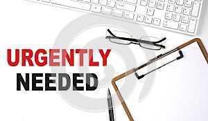 URGENTLY NEEDED text written on white background with keyboard, paper sheet and pen