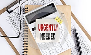 URGENTLY NEEDED word on sticky with clipboard and notebook, business concept