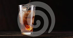 Uring the liquid into the cola glass full of ice cubes. Isolated on dark background