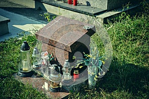 Urn grave with cross on traditional cemetery. Votive candles lantern and flowers on tomb stones in graveyard. All Saints' Day