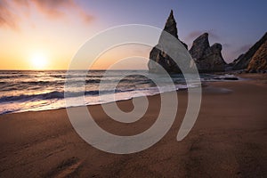 Ursa Beach, Sintra, Portugal. Sand beach with rocks silhouette in evening soft golden sunset light at Atlantic Ocean