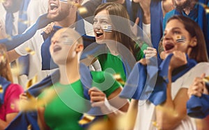 Uruguayan football, soccer fans cheering their team with a blue scarfs at stadium. Excited fans cheering a goal