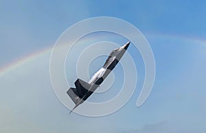 US Airforce F-22 Raptor climbing high with water vapor forming on the wings and a rainbow in the background