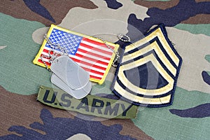 US ARMY Sergeant First Class rank patch, branch tape, flag patch and dog tags on woodland camouflag