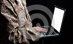 Young soldier working with a laptop computer with blank screen on black background