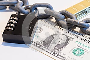 US Dollar banknote under metallic chain with padlock and gold bar in background