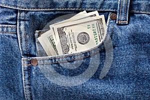 US dollar banknotes in the front left pocket of blue jeans. Concept of saving money or pocket expenses