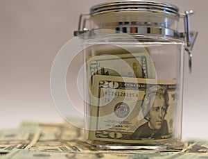 US Dollar bills in Glass Jar with other dollars around in soft focus