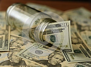 US Dollar bills in Glass Jar with other dollars around in soft focus