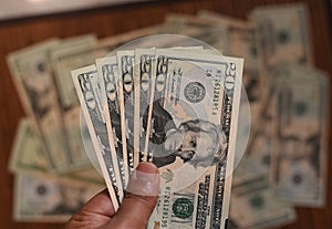 US Dollar bills in human hand with other dollars around in soft focus