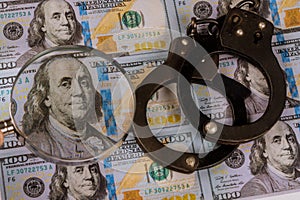 100 US dollars banknotes under magnifying glass of counterfeit money and handcuffs