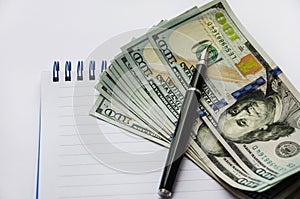 US dollars and a pen on a white notebook