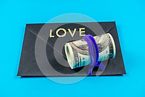 US dollars rolled up and tightened with colored band on light blue background.Sealed black envelop.Love