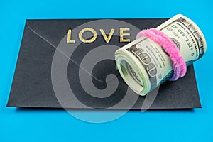 US dollars rolled up and tightened with colored band on light blue background.Sealed black envelop.Love