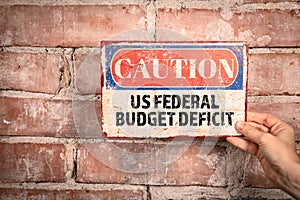 US Federal Budget Deficit. Caution sign in a woman& x27;s hand on a brick background