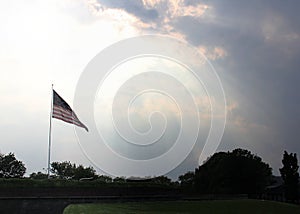 US Flag flying over Fort Jay on Governors Island in sunbeams at dusk, New York