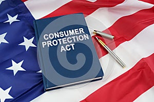 On the US flag lies a pen and a book with the inscription - CONSUMER PROTECTION ACT