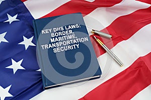 On the US flag lies a pen and a book with the inscription - KEY DHS LAWS - BORDER, MARITIME, TRANSPORTATION SECURITY