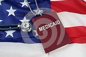 On the US flag lies a stethoscope and a book with the inscription - Medicaid