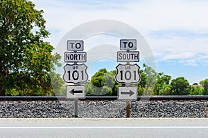 US Highway 101 directional signs. North and South freeway road signs. Background railroad tracks and green trees