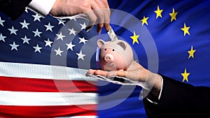 US investment in EU, hand putting money in piggybank on flag background, finance