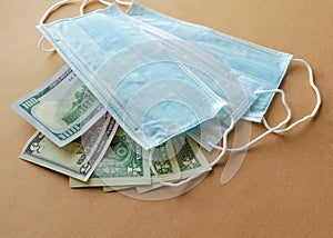 US paper currency with blue medical disposable protective masks on a brown background. Epidemic concept