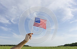 USA flag in hand. Festive USA flag in hand against blue sky and summer natural landscape. American holidays concept.