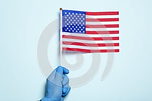 USA medicine and health care concept. A hand in a medical glove holds the US national flag on a light blue background
