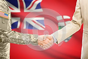 USA military man in uniform and civil man in suit shaking hands with certain Canadian province flag on background - Manitoba