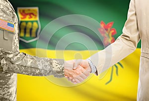 USA military man in uniform and civil man in suit shaking hands with certain Canadian province flag on background - Saskatchewan