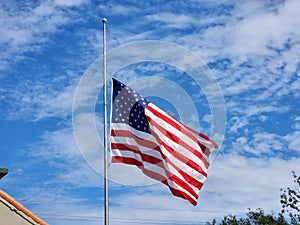 USA national flag waving lowered to half mast on wind against blue sky. American stars and stripes spangled banner as