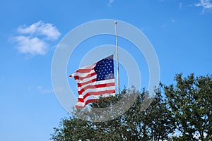 USA national flag waving lowered to half mast on wind against blue sky. American stars and stripes spangled banner as